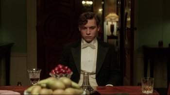Movie still from “An Inspector Calls” (2015), directed by Raymond Pak-Ming Wong – A man in a tuxedo sitting in front of a table; Medium shot, Low angle
