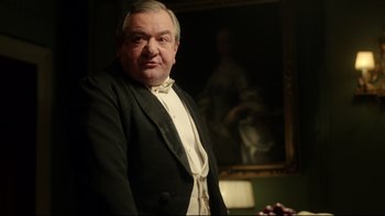 Movie still from “An Inspector Calls” (2015), directed by Raymond Pak-Ming Wong – An older man in a tuxedo posing in front of a painting; Medium shot, Low angle