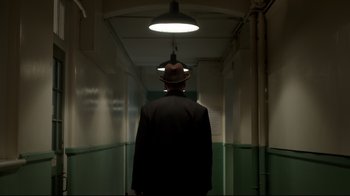 Movie still from “An Inspector Calls” (2015), directed by Raymond Pak-Ming Wong – A man wearing a hat walking down a hall way; Medium shot, Low angle