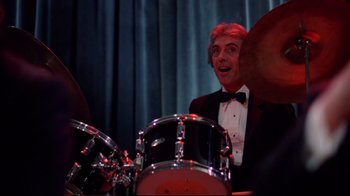 Movie still from “An Officer and a Gentleman” (1982), directed by Taylor Hackford – A man in a tuxedo playing drums in front of a curtain; Medium shot, Over the shoulder angle