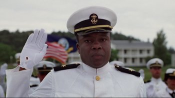 Movie still from “An Officer and a Gentleman” (1982), directed by Taylor Hackford – A man in a white military uniform saluting in front of a flag; Medium shot, Low angle