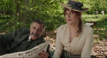 Movie still from “An Officer and a Spy” (2019), directed by Roman Polanski – An older man and woman sitting next to each other holding papers; Medium shot, Low angle