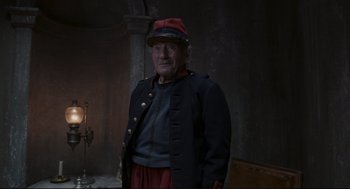 Movie still from “An Officer and a Spy” (2019), directed by Roman Polanski – An old man wearing a red hat and a black jacket; Medium shot, Over the shoulder angle