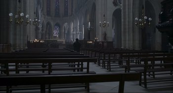 Movie still from “An Officer and a Spy” (2019), directed by Roman Polanski – A man sitting in a pew in a large church; Extreme Wide shot, High angle