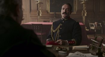 Movie still from “An Officer and a Spy” (2019), directed by Roman Polanski – A man sitting at a table wearing a military uniform; Medium shot, Low angle