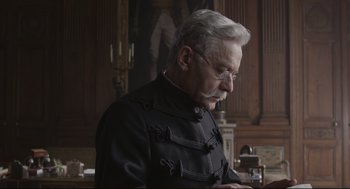 Movie still from “An Officer and a Spy” (2019), directed by Roman Polanski – An older man in a black jacket looking down at a tablet; Close Up shot, Low angle