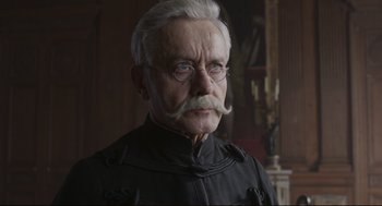 Movie still from “An Officer and a Spy” (2019), directed by Roman Polanski – An old man with a mustache and glasses; Close Up shot, Over the shoulder angle