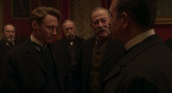 Movie still from “An Officer and a Spy” (2019), directed by Roman Polanski – A group of men standing next to each other in a room; Medium shot, Over the shoulder angle