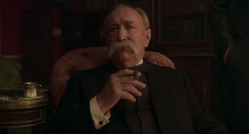 Movie still from “An Officer and a Spy” (2019), directed by Roman Polanski – An older man sitting in a chair smoking a cigarette; Close Up shot, Low angle