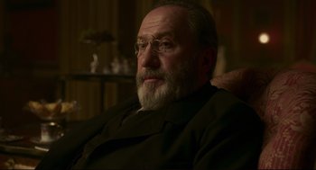 Movie still from “An Officer and a Spy” (2019), directed by Roman Polanski – An old man with a beard and glasses sitting in a chair; Close Up shot, Over the shoulder angle