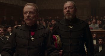 Movie still from “An Officer and a Spy” (2019), directed by Roman Polanski – A couple of men standing next to each other in a room; Close Up shot, Low angle