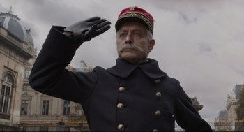Movie still from “An Officer and a Spy” (2019), directed by Roman Polanski – An old man in a uniform saluting in front of a building; Medium shot, Low angle