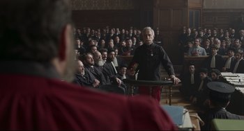 Movie still from “An Officer and a Spy” (2019), directed by Roman Polanski – An old man standing in front of a crowd of people; Medium shot, Over the shoulder angle