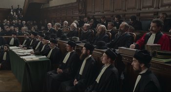 Movie still from “An Officer and a Spy” (2019), directed by Roman Polanski – A group of men sitting in front of each other in a court room; Wide shot, High angle