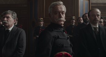 Movie still from “An Officer and a Spy” (2019), directed by Roman Polanski – A group of men standing next to each other in a room; Medium shot, Low angle