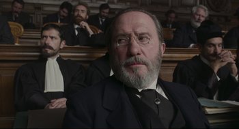 Movie still from “An Officer and a Spy” (2019), directed by Roman Polanski – An old man with a beard in a courtroom; Close Up shot, Low angle