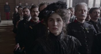 Movie still from “An Officer and a Spy” (2019), directed by Roman Polanski – A group of people standing around a woman in a black dress; Close Up shot, Over the shoulder angle