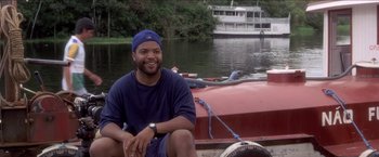 Movie still from “Anaconda” (1997), directed by Luis Llosa – A man sitting in front of a boat on a river; Medium shot, Low angle