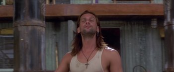 Movie still from “Anaconda” (1997), directed by Luis Llosa – A man with long brown hair wearing a white tank top and a cross necklace; Close Up shot, Low angle