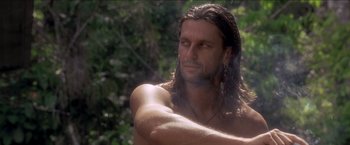 Movie still from “Anaconda” (1997), directed by Luis Llosa – A man with long brown hair and a bare chest; Close Up shot, Low angle