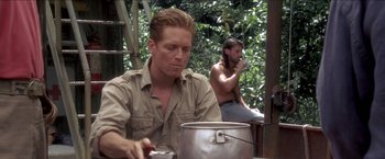 Movie still from “Anaconda” (1997), directed by Luis Llosa – A man sitting in front of a pot while another man sits in the background; Medium shot, Low angle