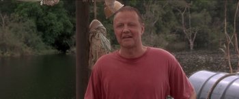 Movie still from “Anaconda” (1997), directed by Luis Llosa – A man standing next to a pole with a bird hanging from it; Close Up shot, Low angle