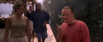 Movie still from “Anaconda” (1997), directed by Luis Llosa – A man eating a piece of food while standing next to two other people; Medium shot, Low angle
