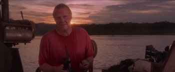 Movie still from “Anaconda” (1997), directed by Luis Llosa – An older man is holding a hammer by the water; Medium shot, Low angle