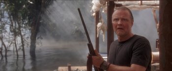 Movie still from “Anaconda” (1997), directed by Luis Llosa – An older man holding a rifle in front of a body of water; Medium shot, Low angle