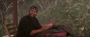 Movie still from “Anaconda” (1997), directed by Luis Llosa – A man sitting on the ground holding a pair of shoes; Medium shot, High angle