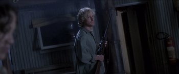 Movie still from “Anaconda” (1997), directed by Luis Llosa – A man holding a rifle in a dark room; Medium shot, Low angle