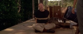 Movie still from “Anaconda” (1997), directed by Luis Llosa – A man sitting on the ground tied to a rope; Medium shot, Over the shoulder angle