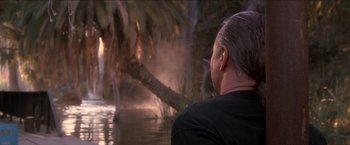 Movie still from “Anaconda” (1997), directed by Luis Llosa – A man in black shirt looking out over a body of water; Wide shot, Over the shoulder angle