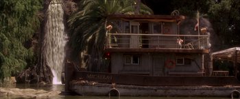 Movie still from “Anaconda” (1997), directed by Luis Llosa – A boat in a body of water next to palm trees; Extreme Wide shot, Low angle