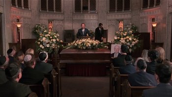 Movie still from “Analyze That” (2002), directed by Harold Ramis – A man standing at the top of a casket in front of people; Wide shot, Low angle