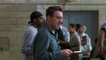 Movie still from “Analyze That” (2002), directed by Harold Ramis – A man holding a plate in front of a group of people; Medium shot, Over the shoulder angle