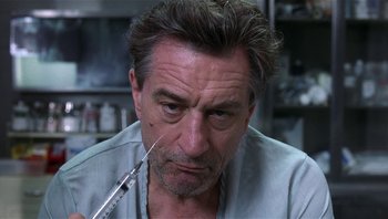 Movie still from “Analyze That” (2002), directed by Harold Ramis – A person with a syringe in his mouth; Close Up shot, Low angle