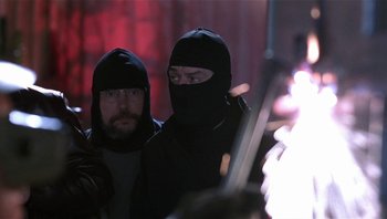 Movie still from “Analyze That” (2002), directed by Harold Ramis – Two men in black balaclavas are standing next to a fire; Medium shot, Low angle