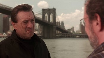 Movie still from “Analyze That” (2002), directed by Harold Ramis – A man standing in front of a river with a bridge in the background; Close Up shot, Low angle