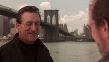Movie still from “Analyze That” (2002), directed by Harold Ramis – A man standing in front of a river with a bridge in the background; Close Up shot, Low angle