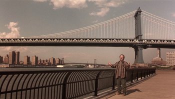 Movie still from “Analyze That” (2002), directed by Harold Ramis – A man standing next to a bridge with a city in the background; Wide shot, Low angle