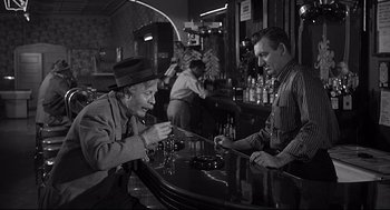 Movie still from “Anatomy of a Murder” (1959), directed by Otto Preminger – Two men sitting at a table in front of a bar; Medium shot, Over the shoulder angle
