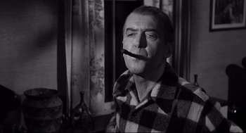 Movie still from “Anatomy of a Murder” (1959), directed by Otto Preminger – An older man wearing a plaid shirt and holding a pipe in his mouth; Medium shot, Over the shoulder angle