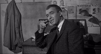Movie still from “Anatomy of a Murder” (1959), directed by Otto Preminger – A man sitting at a desk smoking a cigarette; Medium shot, Over the shoulder angle