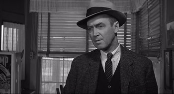 Movie still from “Anatomy of a Murder” (1959), directed by Otto Preminger – A man wearing a suit and a hat in front of a window; Close Up shot, Over the shoulder angle