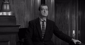 Movie still from “Anatomy of a Murder” (1959), directed by Otto Preminger – A man sitting in a chair wearing a suit and tie; Medium shot, Low angle