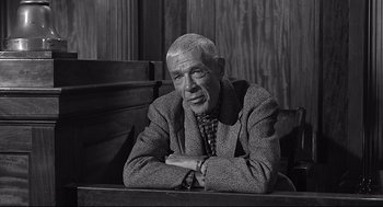 Movie still from “Anatomy of a Murder” (1959), directed by Otto Preminger – An older man sitting at a table with his arms crossed; Medium shot, Low angle
