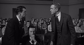 Movie still from “Anatomy of a Murder” (1959), directed by Otto Preminger – A group of people in a room with a crowd of people in the background; Medium shot, Over the shoulder angle