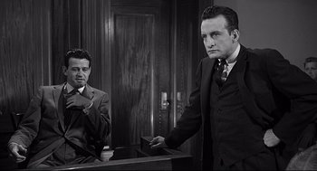 Movie still from “Anatomy of a Murder” (1959), directed by Otto Preminger – A man in a suit and tie standing next to another man in a suit and tie; Medium shot, Low angle