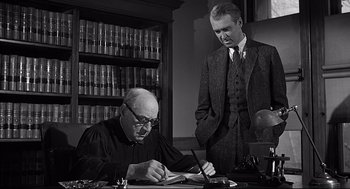Movie still from “Anatomy of a Murder” (1959), directed by Otto Preminger – Two men in suits are writing at a desk; Medium shot, Low angle